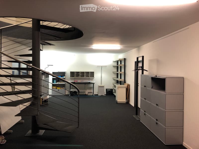 Modern office space with a spiral staircase, a desk with a chair, shelves, and cabinets.