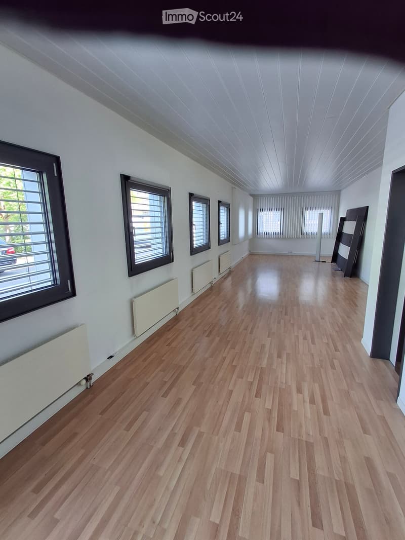 Empty room with wooden flooring, white walls, large windows, radiators, and a tall white column.