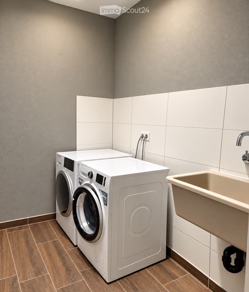 Bathroom with a washing machine and a sink, featuring wooden flooring and tiled walls.
