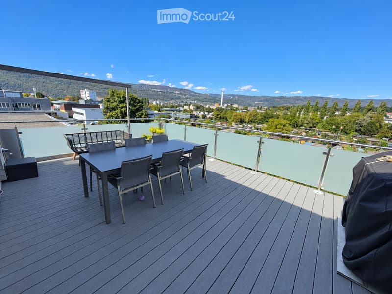 Wooden deck with a black dining table and chairs, a covered grill, and a view of the city and mountains.