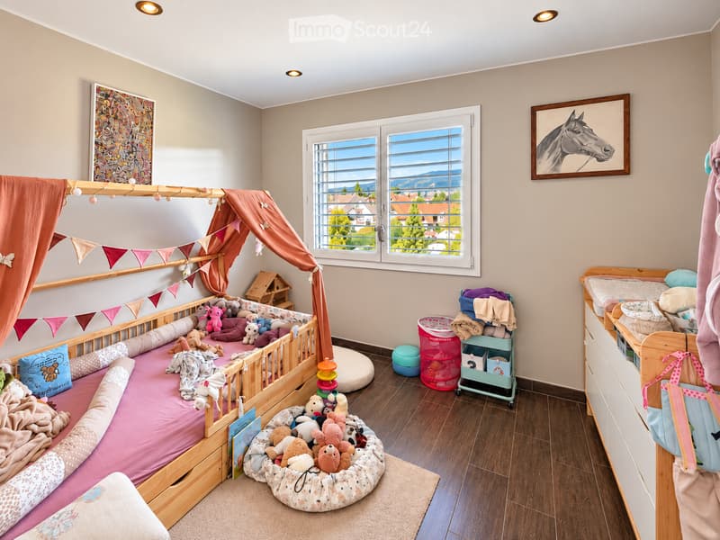 Cozy children's bedroom with a wooden bed, colorful toys, a play tent, and a view of the mountains through large windows.