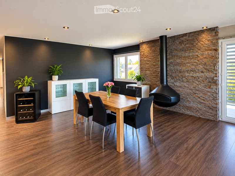 Modern dining room with wooden flooring, a large wooden dining table surrounded by black chairs, a wine cabinet, a white display cabinet, and a stone wall with a built-in fireplace.