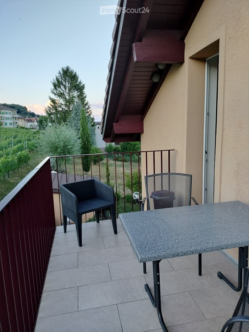 Balcony with tiled floor, wooden railing, and outdoor furniture including a chair and table.