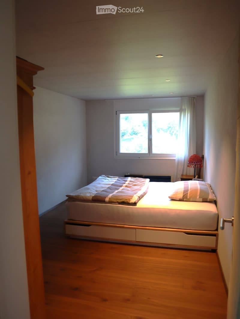 Minimalist bedroom with a single bed, wooden floor, and a window with sheer curtains.