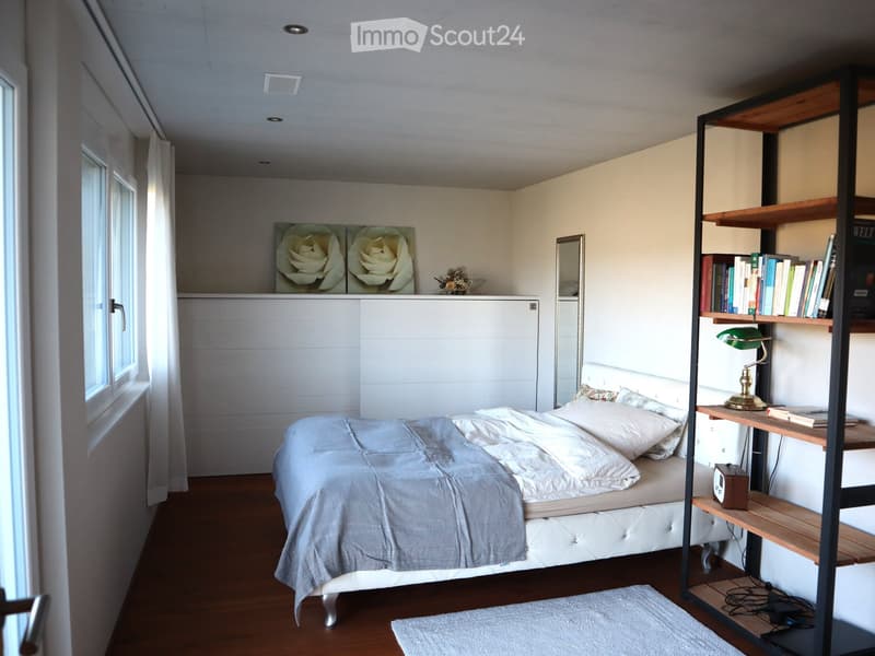 Cozy bedroom with a white bed, wooden shelves, a green desk lamp, and a mirror on the wall.