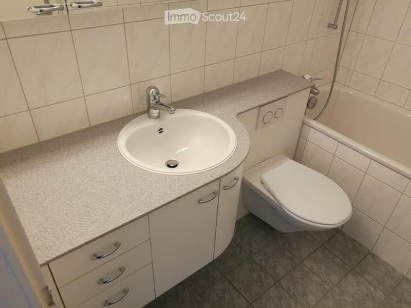 Modern bathroom with a white sink, chrome faucet, built-in cabinet, and toilet. Light-colored tiles on walls and floor.