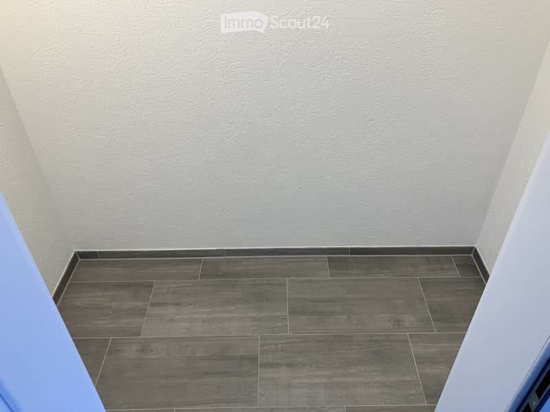 Empty room with grey textured walls and dark grey tiled floor, no furniture or equipment visible.