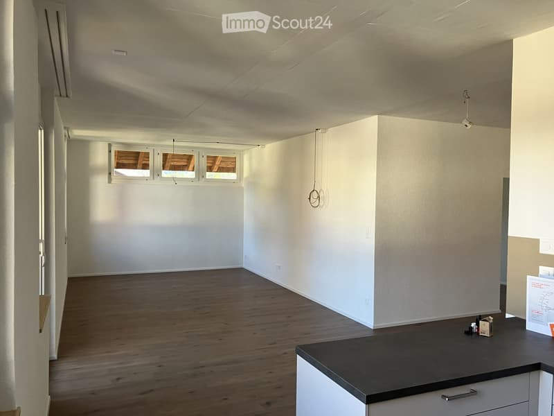 Empty room with wooden flooring, white walls, and a window with three panes. There is a small counter with a few items on it, but no furniture.