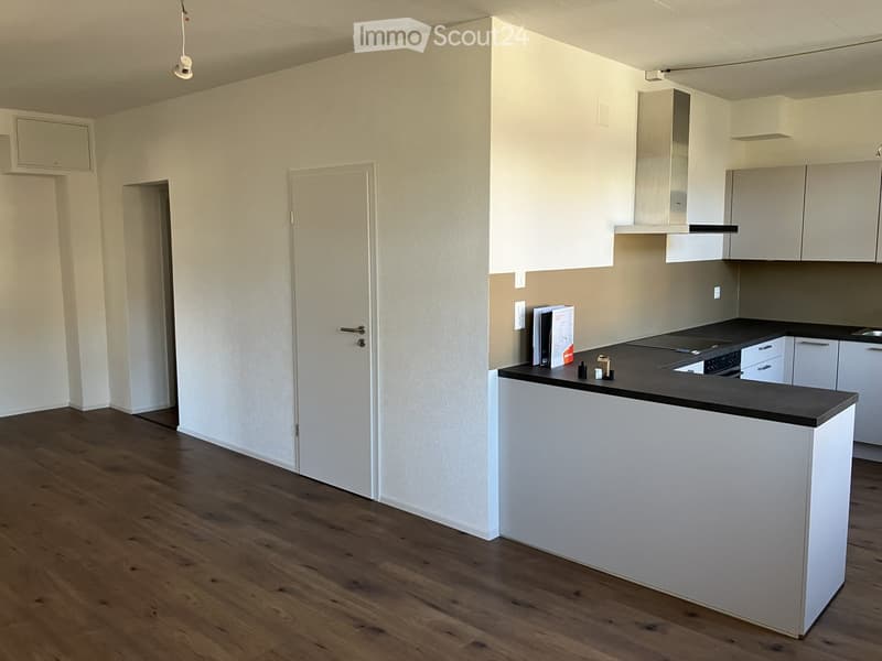 Modern kitchen with white cabinets, dark countertop, and wooden flooring. Features an oven, faucet, and a small island.