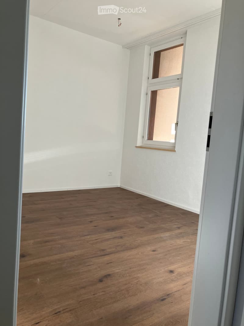 Empty room with wooden flooring and white walls, featuring a window with a white frame and a small shelf below it.