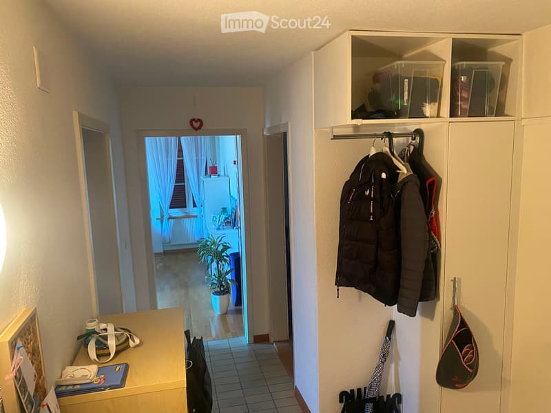Hallway with a coat rack, small table, and an open door leading to another room with a plant and a window.