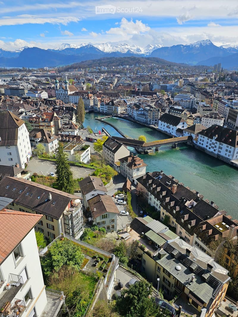 Aerial view of a city with many buildings, a river, a bridge, cars parked on the sides, mountains in the distance