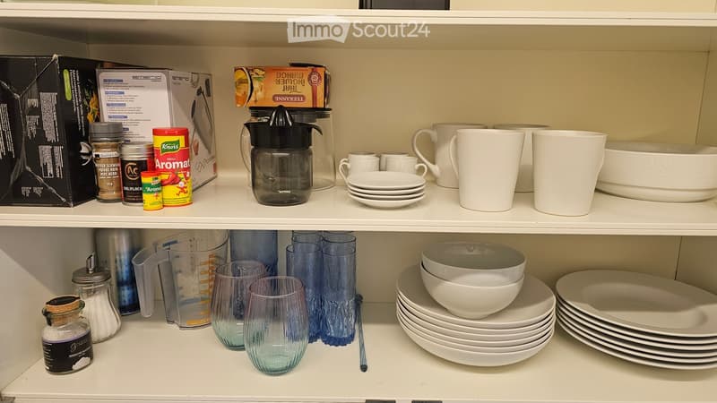 kitchenware on shelves including glasses, bowls, measuring cups, pitchers, and jars
