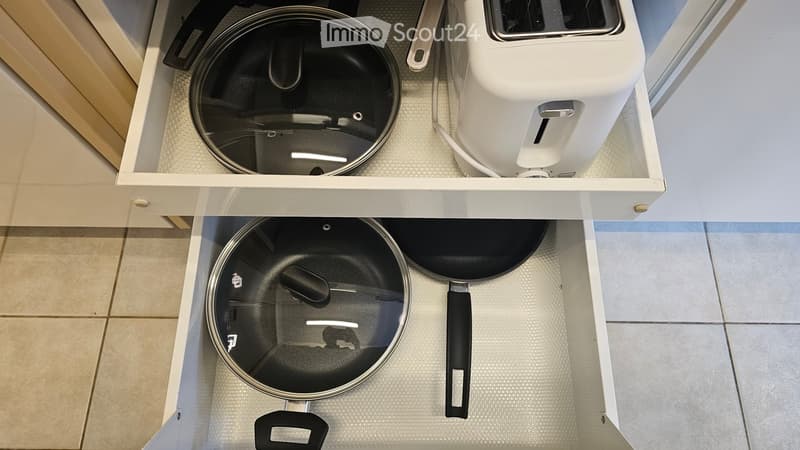 Two drawers of a kitchen with a pot, pans and a toaster inside