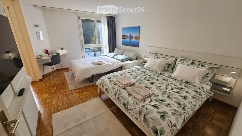 Two double beds, desk, window, framed picture, lamp, rug, wooden floor