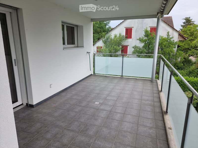 Balcony with tiled floor, glass railing, and a view of neighboring houses and greenery.