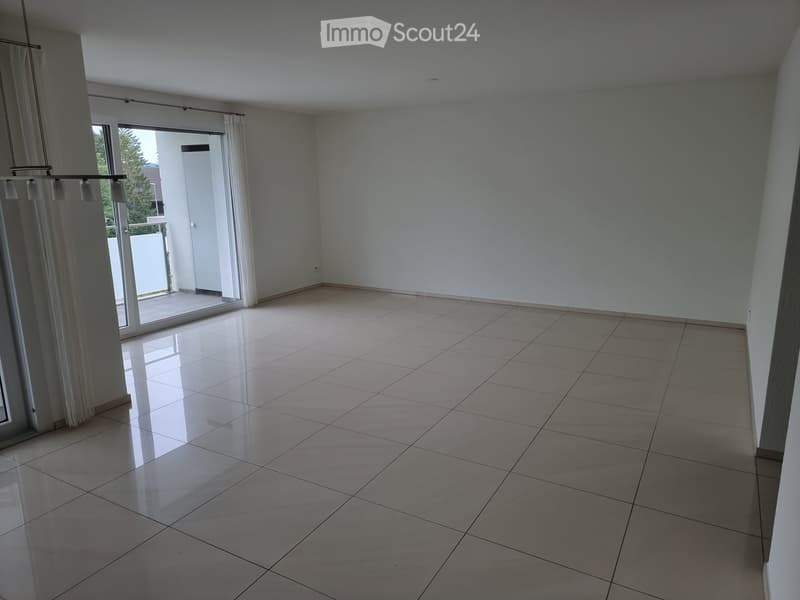 Empty room with tiled floor, large window with white curtains, and a sliding glass door leading to a balcony.