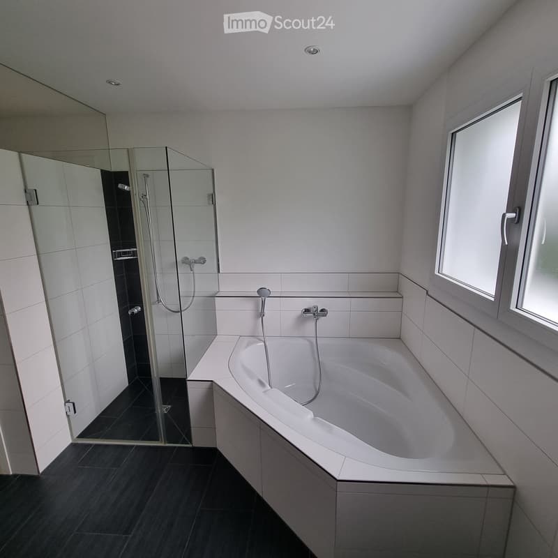 Modern bathroom with a white bathtub, glass-enclosed shower, and sleek fixtures.