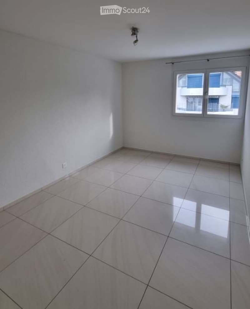 Empty room with white tiled floor and white walls, featuring a single window with white frame and a ceiling light fixture.