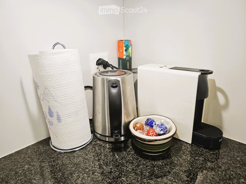 A kitchen countertop with a paper towel holder, a coffee maker, a bowl of candies, and a cup.