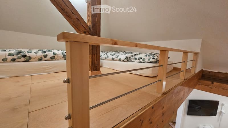 Loft-style bedroom with wooden staircase leading to a lofted sleeping area featuring a bed with a leafy-patterned duvet and pillows.