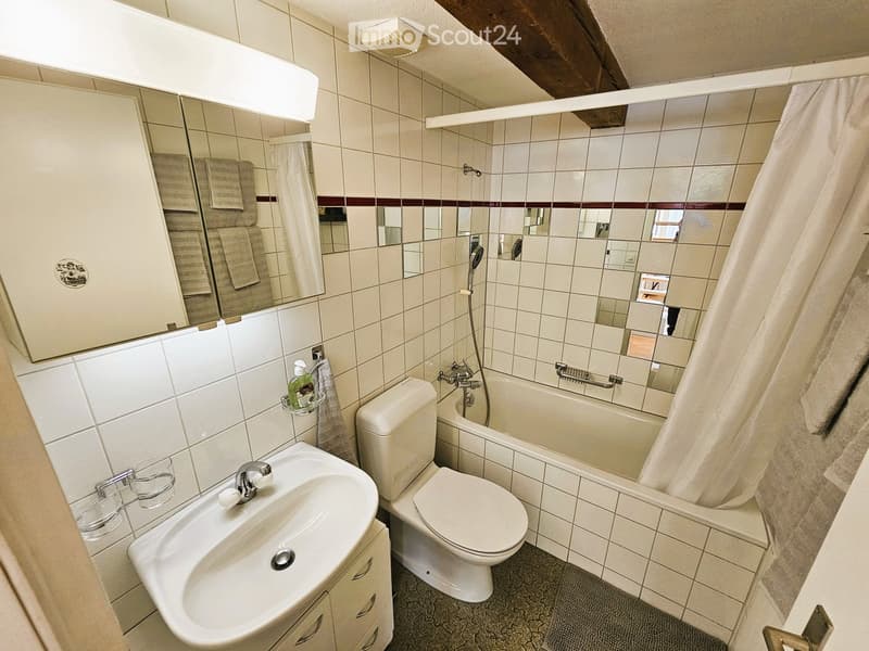 Bathroom with white tiles, a sink, toilet, bathtub, and a large mirror with towels hanging on either side.