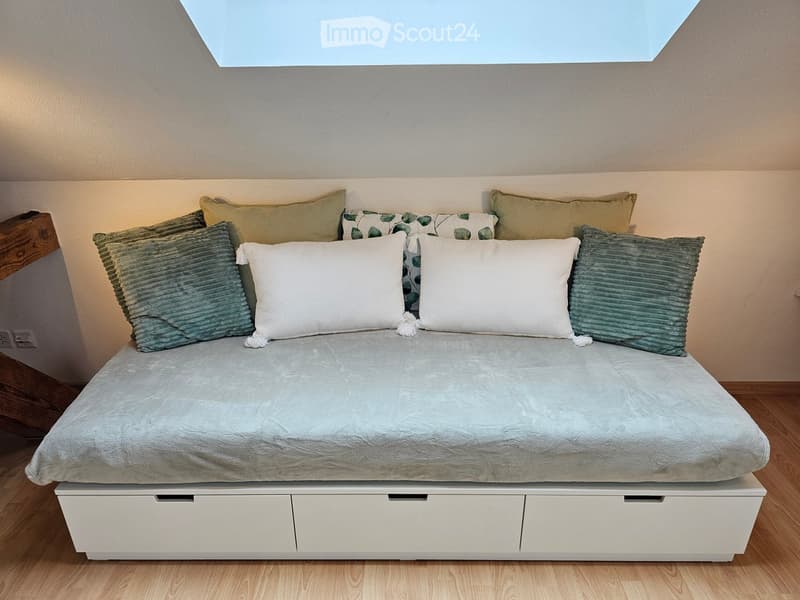 A modern bedroom with a neatly made bed, multiple pillows, and built-in storage drawers beneath the bed.
