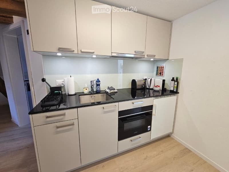 Modern kitchen with white cabinets, black countertop, stainless steel sink, built-in oven, and various small appliances.