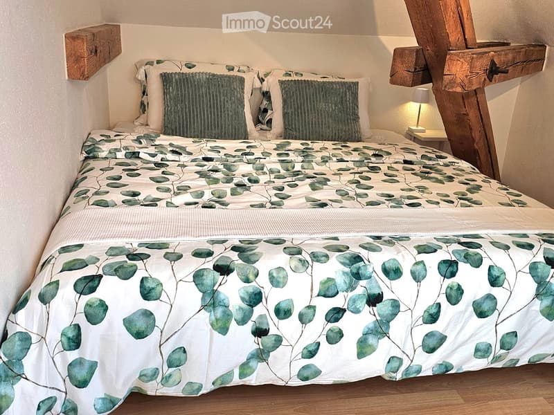 Cozy bedroom with a double bed featuring a green leaf-patterned duvet, two matching pillows, and a wooden nightstand with a lamp.