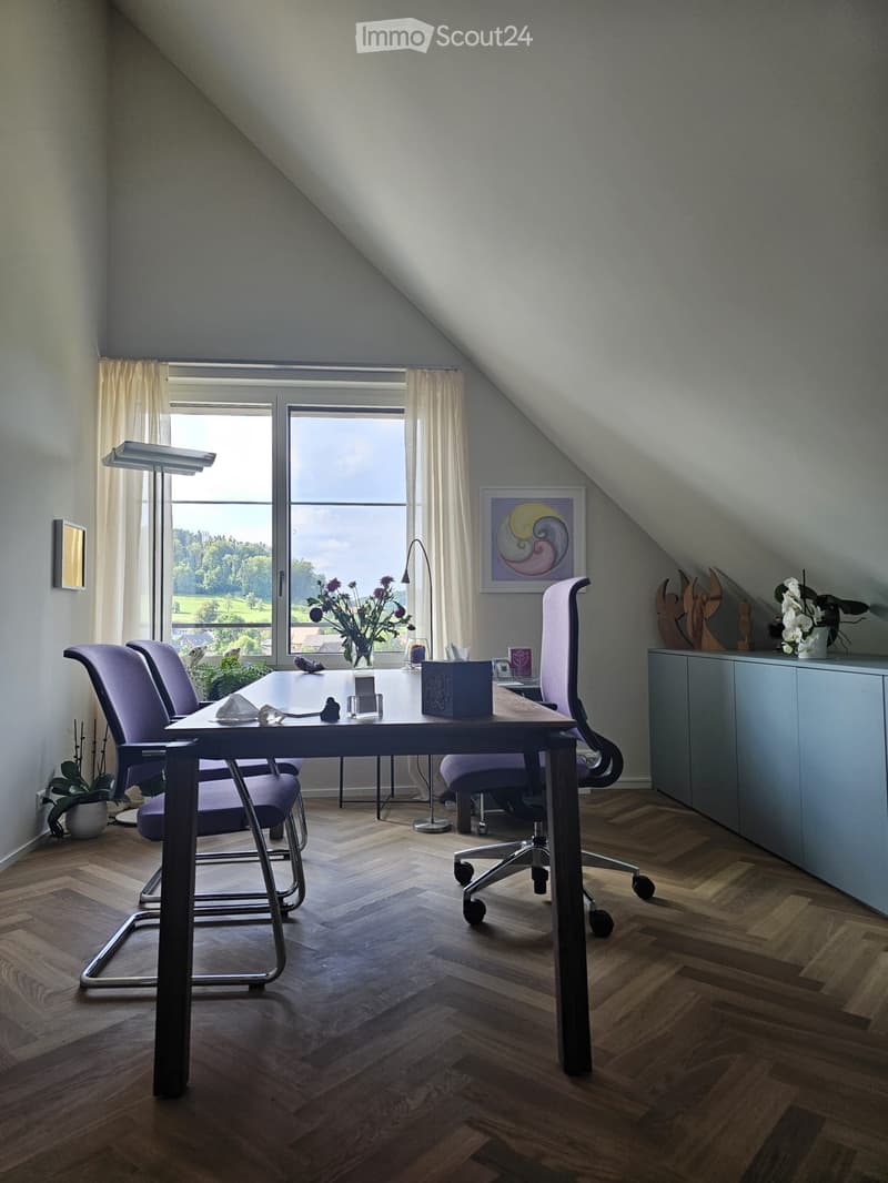 Modern office space with wooden herringbone flooring, large window with view, purple chairs, desk, and decorative items.