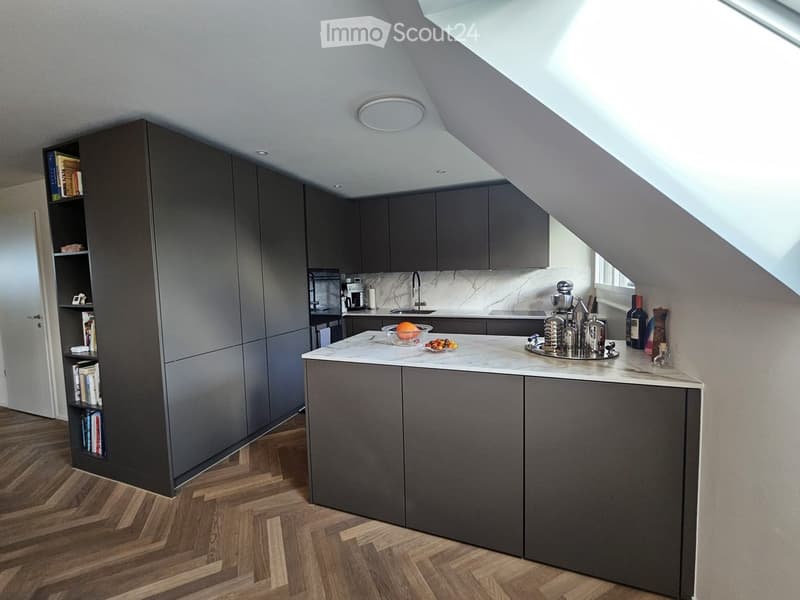 Modern kitchen with dark grey cabinets, marble countertop, and wooden flooring. Features a sink, coffee maker, and decorative items on the counter.
