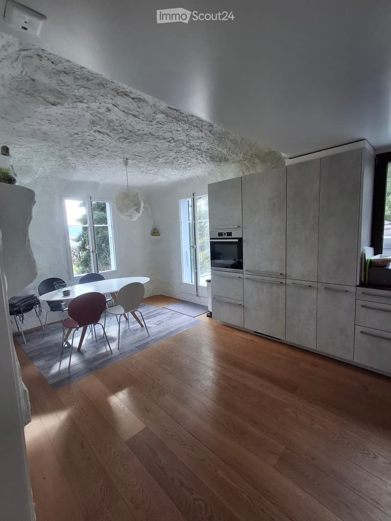 Modern kitchen with light grey cabinets, a dining area with a white table and colorful chairs, and a wooden floor.