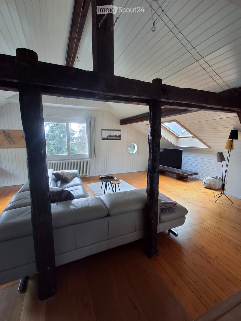 Living room with exposed wooden beams, hardwood floor, grey sectional sofa, coffee table, TV, and floor lamp.