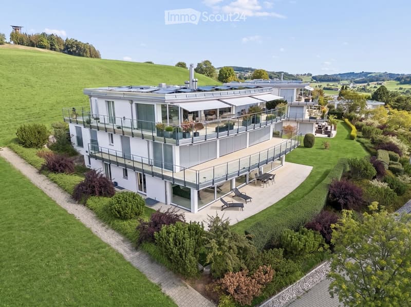 Modern two-story house with large balconies, surrounded by a well-maintained garden and lawn area.