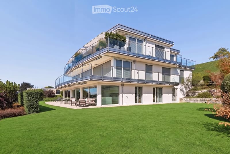 Modern two-story house with large windows, balconies, and a well-maintained lawn in front.