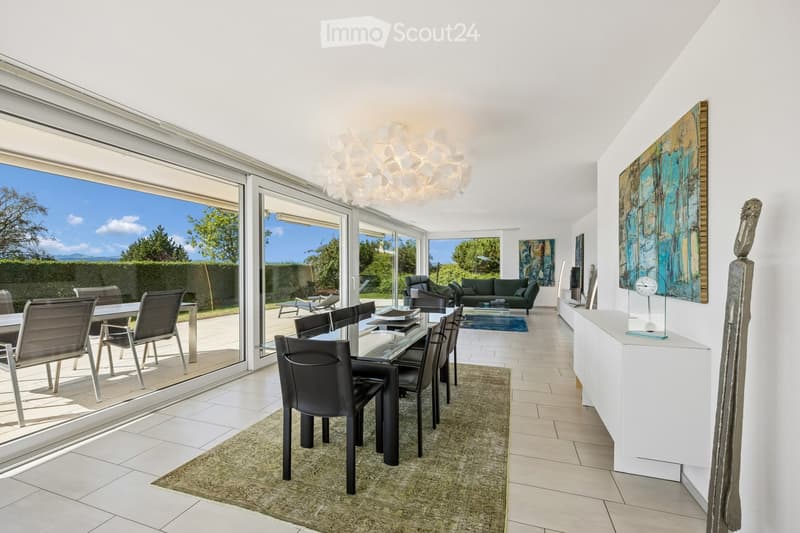 Bright, open-plan living and dining area with large glass doors leading to a patio, featuring a modern dining set, a green sofa, and contemporary wall art.