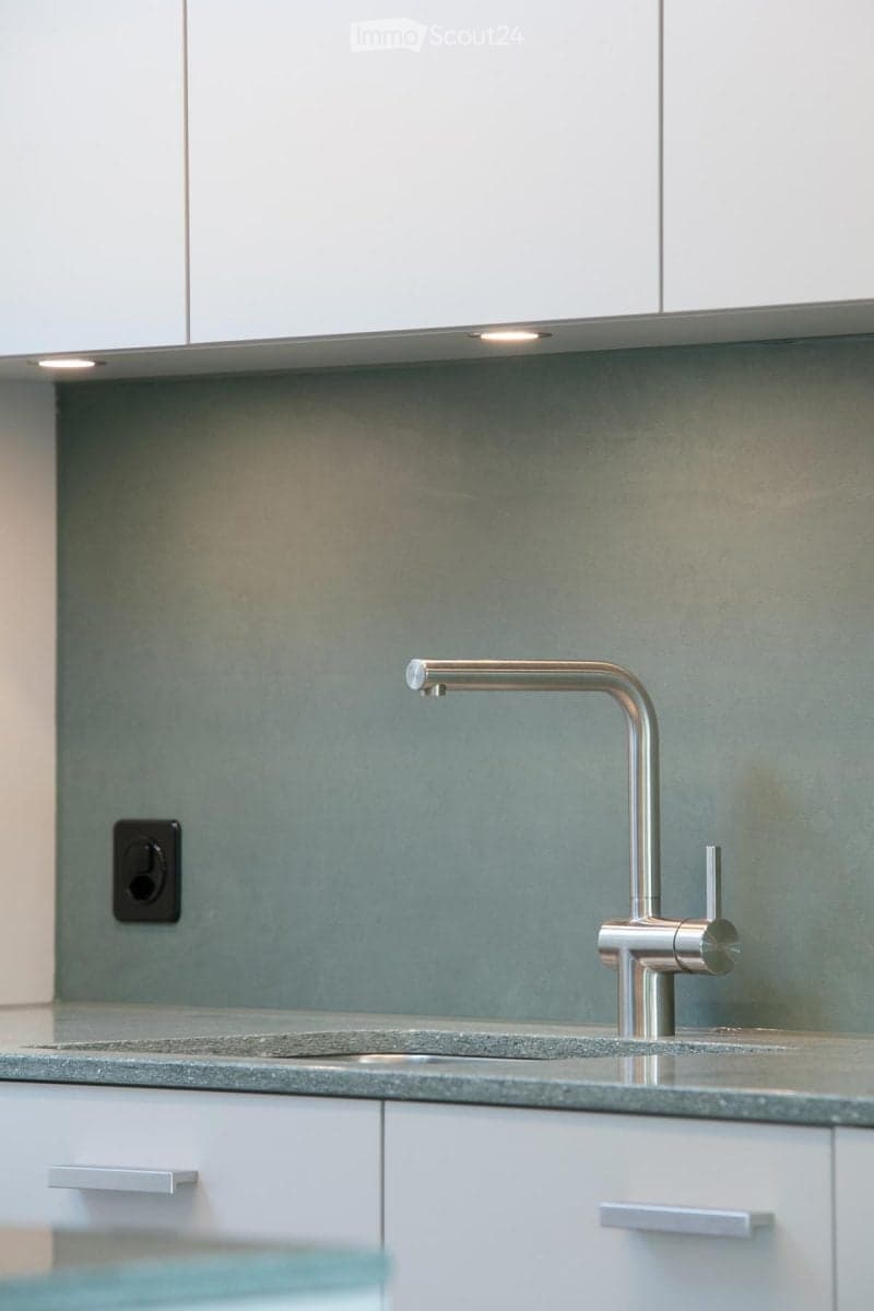 Modern kitchen with a sleek, stainless steel faucet, a grey countertop, and white cabinets.