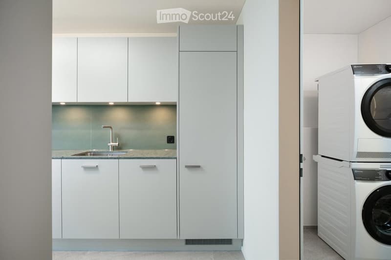 Modern bathroom with white cabinets, a sink, and a private washing machine in the corner.