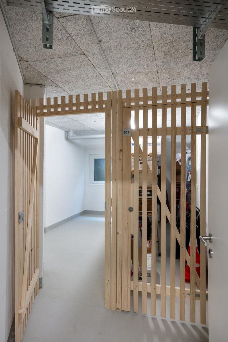 A modern hallway with a wooden gate featuring a decorative fence design, leading to another room with visible storage and items.