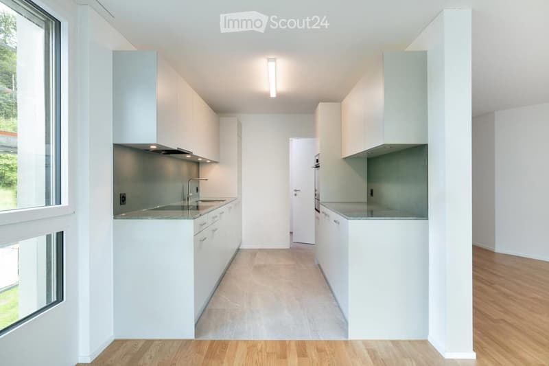 Modern, minimalist kitchen with white cabinets, a central island, and a sink area. The space features light-colored countertops, a sleek faucet, and ample natural light from large windows.