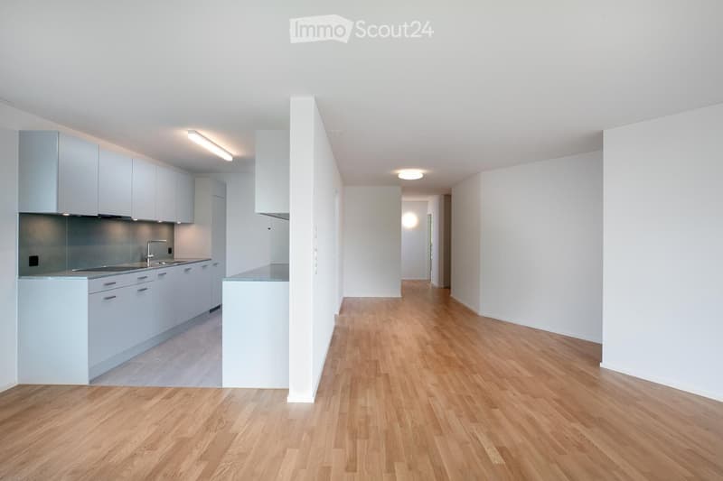 Open-plan kitchen and living area with light-colored cabinets, a central island, and wooden flooring.