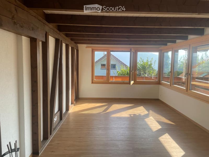 Empty room with wooden flooring, large windows, and exposed wooden beams on the ceiling.