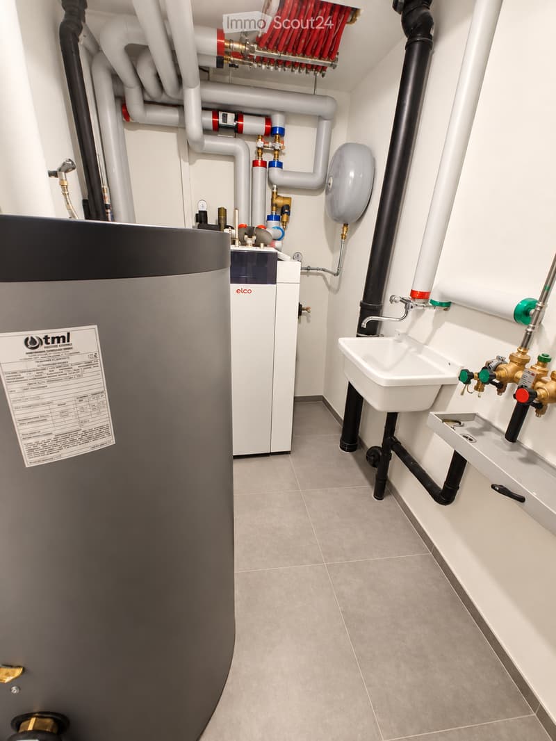 Modern bathroom utility area with a white sink, faucet, water heater, and exposed pipes.