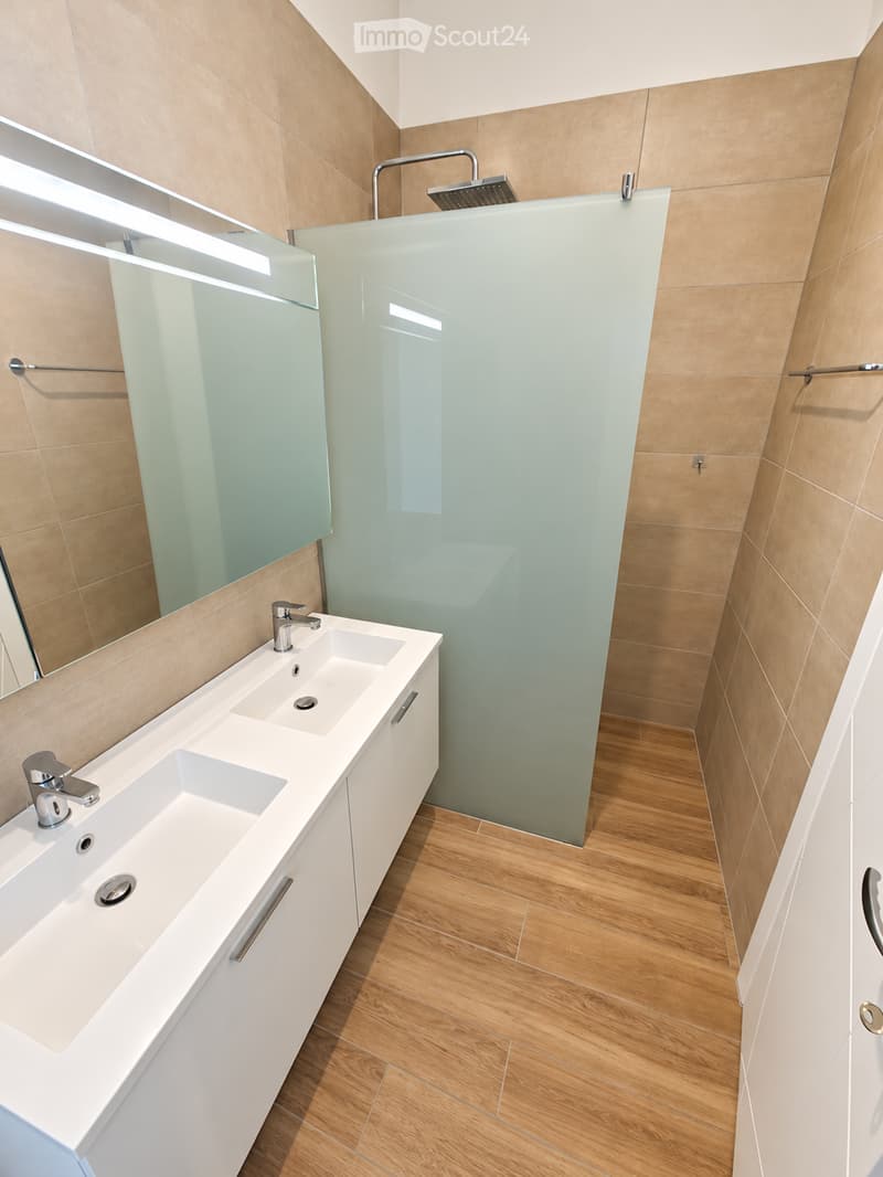 Modern bathroom with a double sink, sleek white cabinetry, a large mirror, and a glass-enclosed shower area with a modern showerhead.