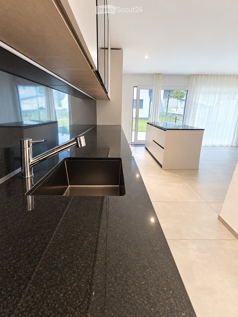Modern kitchen with black granite countertops, stainless steel sink and faucet, white cabinets, and large windows with white curtains.