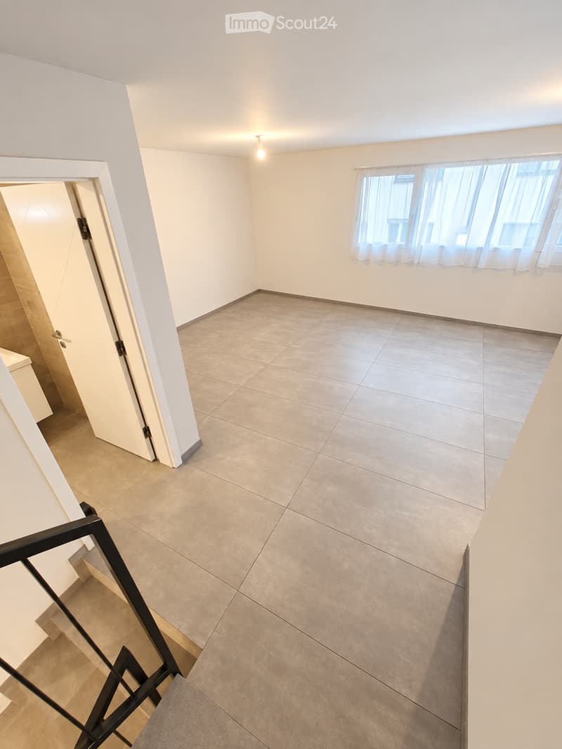 Empty room with tiled floor, white walls, and large windows with curtains. A staircase leads to another level.
