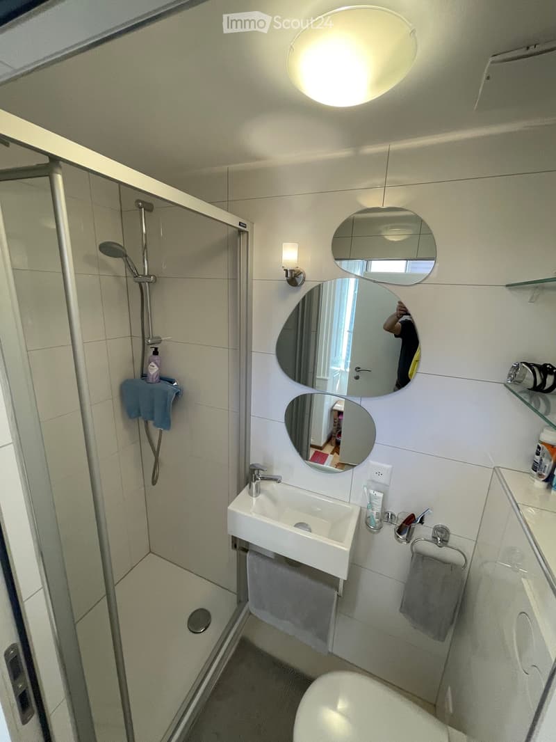 Modern bathroom with white tiles, a sink, a toilet, a shower, and a mirrored wall with multiple round mirrors.
