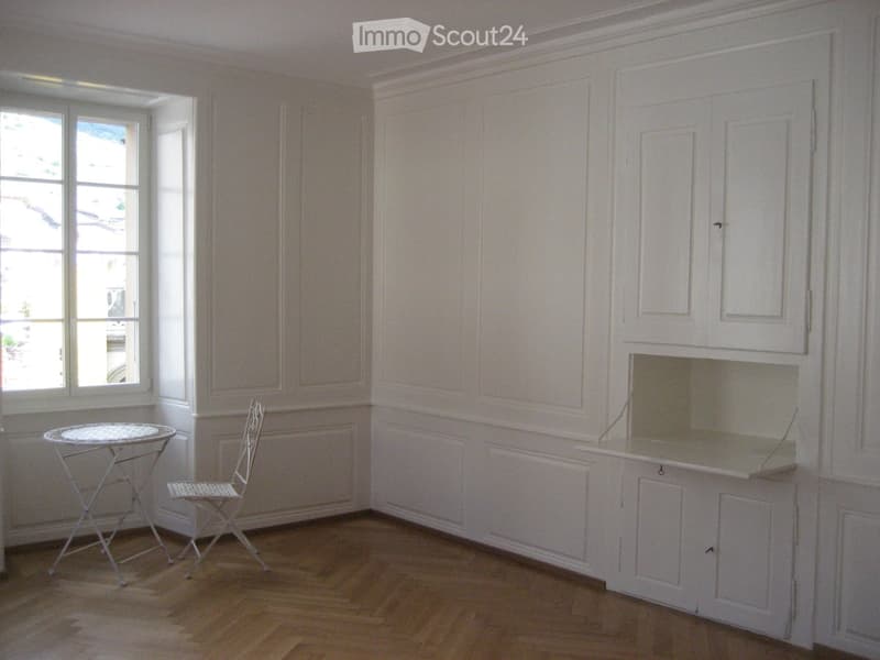Bright room with wooden flooring, white cabinetry, a small round table, and a matching chair near a large window.