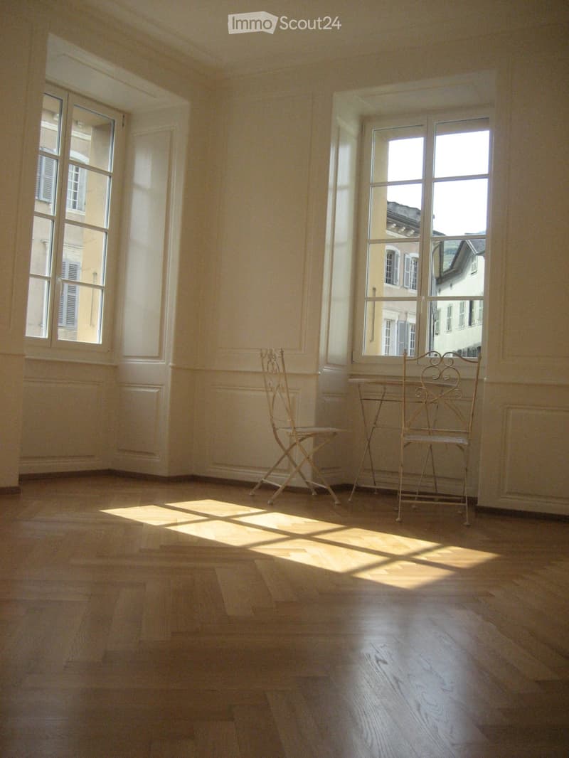 Bright, unfurnished room with wooden flooring, large windows, and two chairs near the windows.