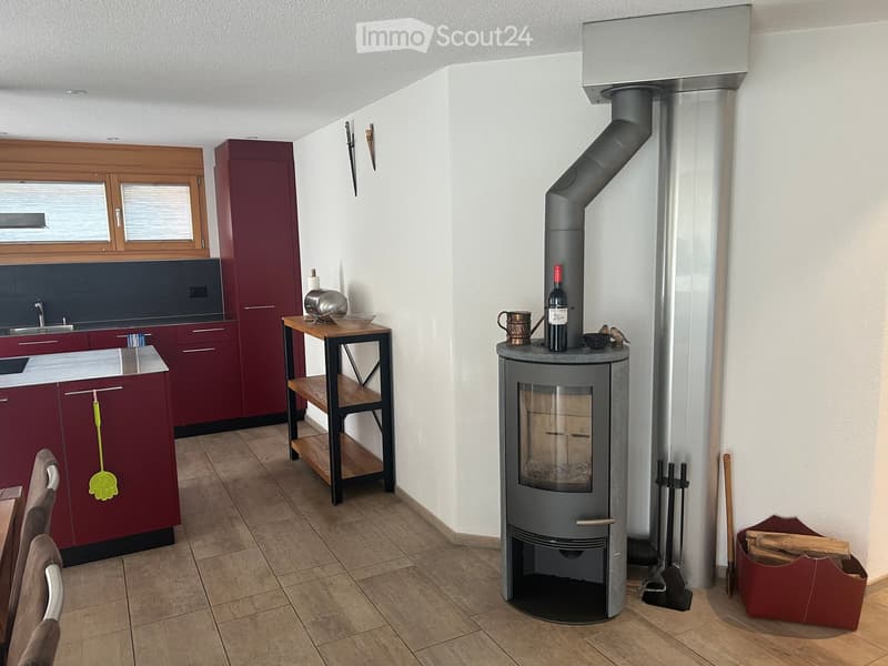 Modern kitchen with dark red cabinets, a stainless steel sink, a small wooden stool, and a wood-burning stove with a chimney.